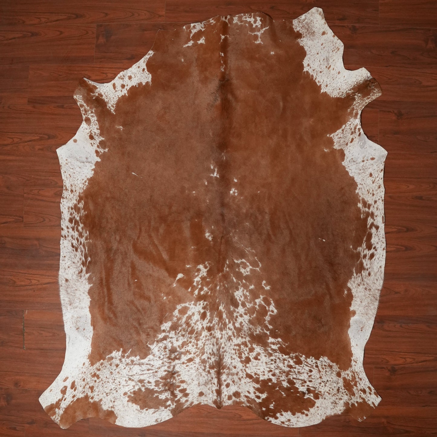 Brown cowhide rug with white patches on a wooden floor