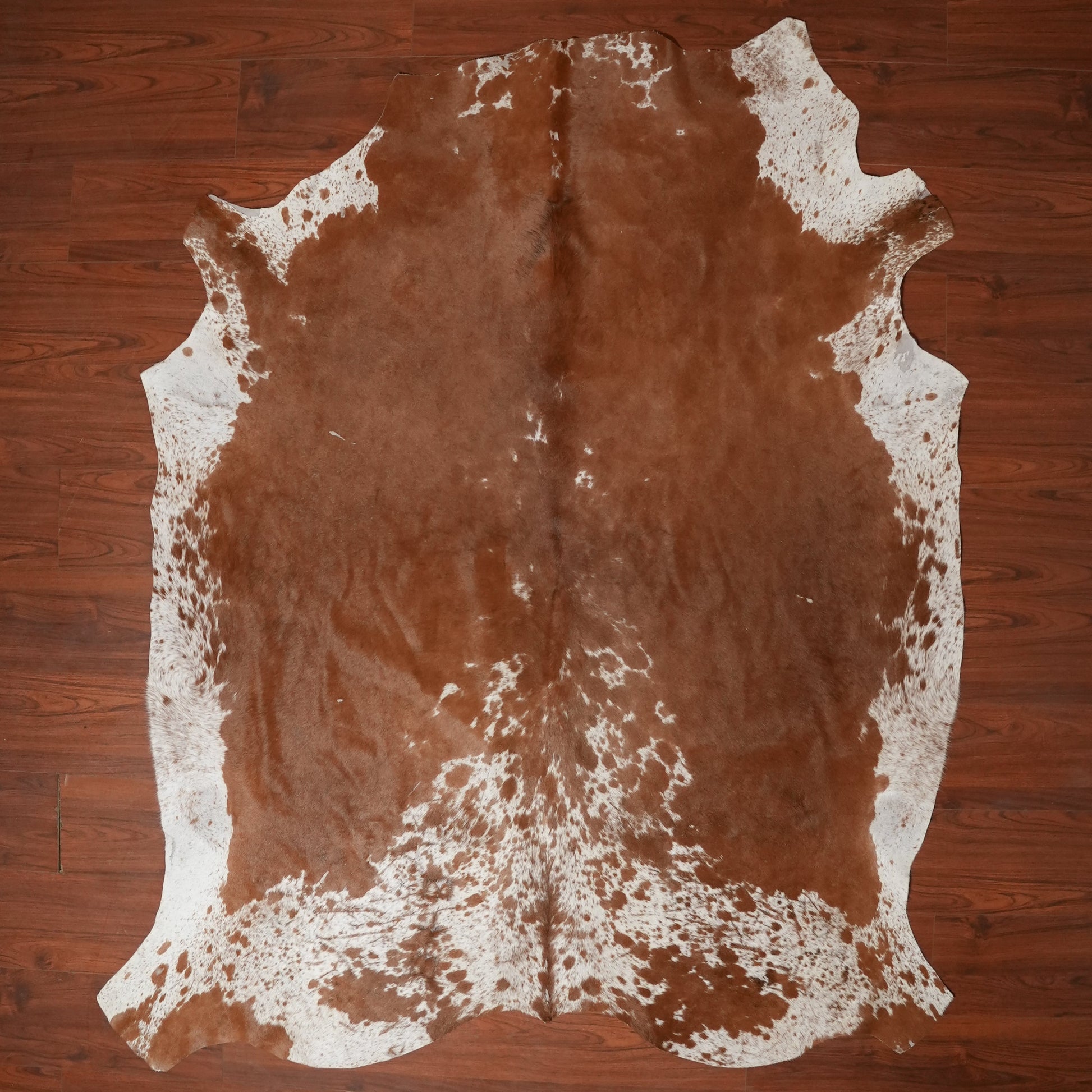 Brown cowhide rug with white patches on a wooden floor
