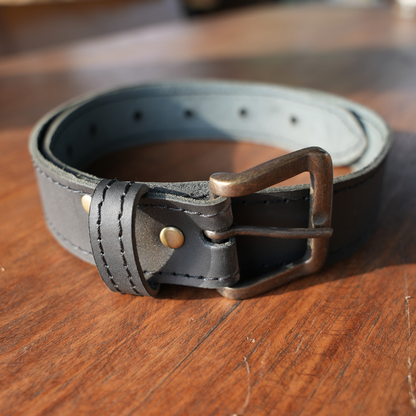 A black leather belt with a bronze-toned metal buckle, resting on a wooden surface.