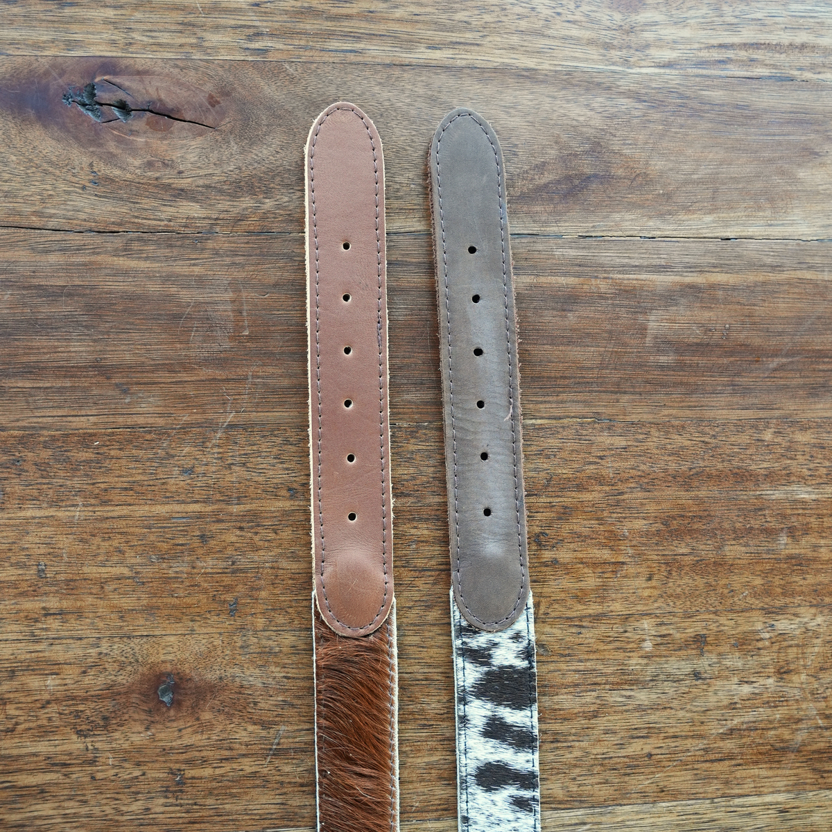 Two leather belt strap ends laid flat on a rustic wooden surface. 
