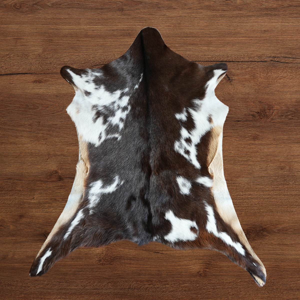 A goat hide with a dark brown and white spotted pattern, laid flat on a warm brown wooden surface.