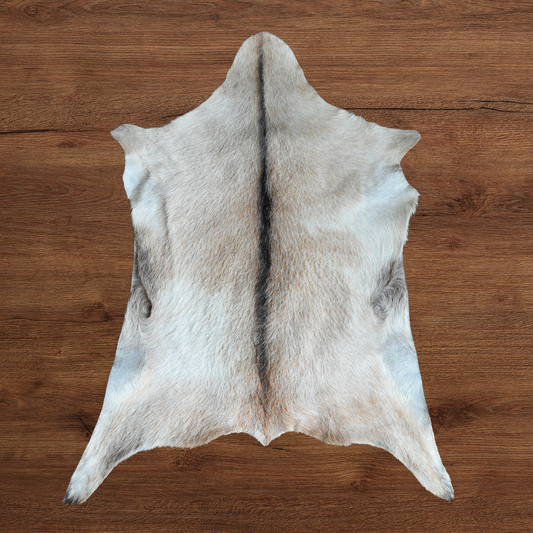 A pale cream and grey goat hide with a central dark stripe, laid flat on a brown wooden surface.